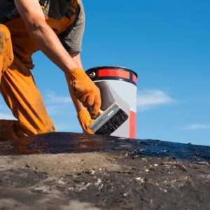 Roofer cover the concrete base, polymer modified bitumen waterproofing primer. A worker brushes cover concrete, bitumen-rubber primer.